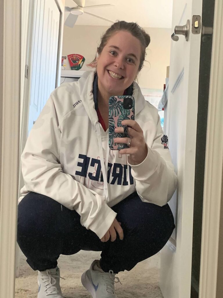 Emily wearing a white sweatshirt, blue joggers, and white tennis shoes while holding her phone